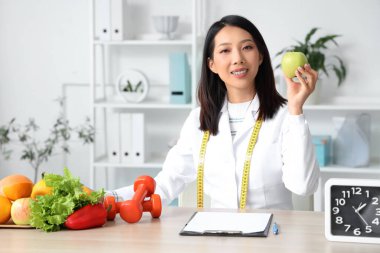 Ofisinde elma bulunan Asyalı kadın beslenme uzmanı.