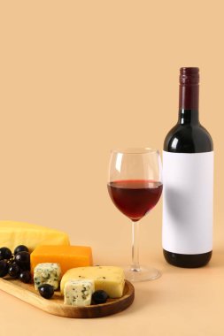 Lezzetli peynirli ahşap tahta, üzüm, şişe ve bej arka planda bir bardak şarap.