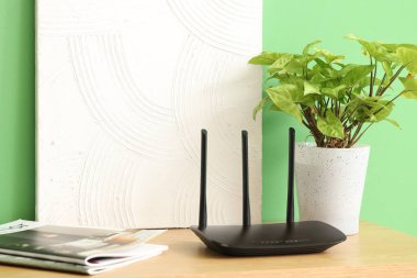 Yeşil duvarın yanındaki rafta bitki, dergi ve boya ile modern wi-fi yönlendirici