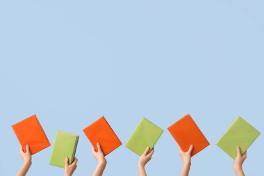 Açık mavi arkaplanda kitapları tutan eller