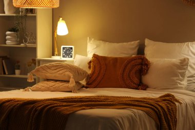 Geceleri battaniyeli, yastıklı ve komodinli rahat bir yatak.