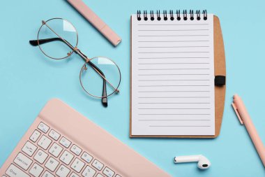 Mavi zemin üzerinde defter, gözlük ve klavye olan kompozisyon. Yakın çekim.