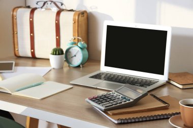 Hesap makinesi, not defteri ve beyaz duvarın yanındaki modern dizüstü bilgisayarı olan rahat bir iş yeri