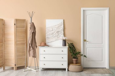 Giysileri, çekmeceleri ve bej duvarın yanındaki resmi olan şık bir salonun içinde.