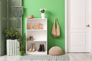 Salonun içinde raf ünitesi, bir buket çiçek ve yeşil duvarda çanta.