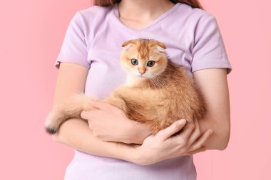 Pembe arka planda sevimli kedi yavrusu olan genç bir kadın.