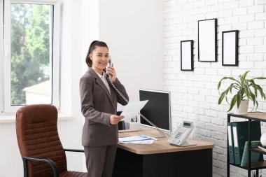 Kadın ofis çalışanı şık bir ofiste iş yerinin yakınında telefonla konuşuyor.