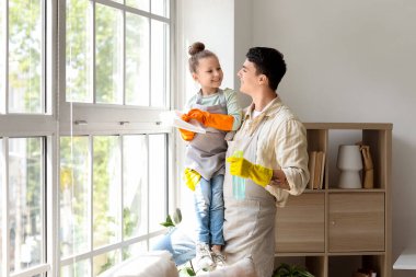 Genç baba ve kızı evde birlikte cam temizliyorlar.