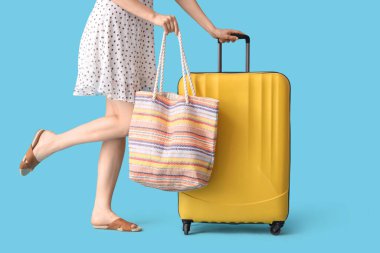 Mavi arka planda bavulu ve çantası olan genç bir kadın.