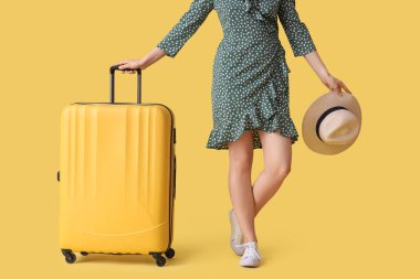Sarı arka planda bavulu ve şapkası olan genç bir kadın.