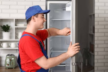 Mutfaktaki buzdolabını tamir eden mutlu erkek işçi.