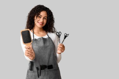 Gri arka planda fırça ve makasla güzel, mutlu, Afro-Amerikan kuaför.