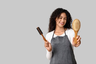 Gri arka planda fırçaları olan güzel, mutlu, Afro-Amerikalı bir kuaför.