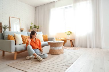 Evde dizüstü bilgisayar kullanan güzel bir genç kadın.