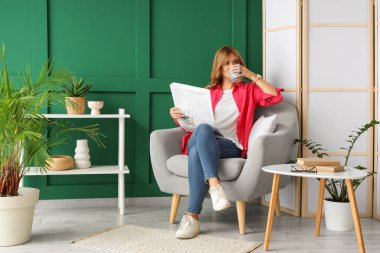 Elinde gazete ve bir fincan çayla evdeki koltukta oturan genç ve güzel bir kadın.