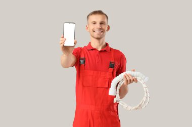 Cep telefonu ve arka planda hortumları olan erkek tesisatçı.