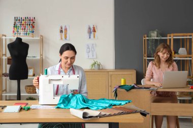 Atölyedeki masada kadın terzi dikiş dikiyor.