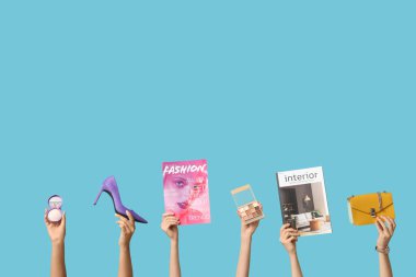 Farklı dergilere sahip kadın elleri, yüksek topuklu ayakkabılar, şık çanta ve mavi arka planda dekoratif kozmetik ürünler.