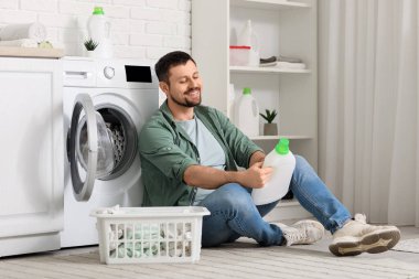 Çamaşır makinesinin yakınındaki çamaşır deterjanı tarifini okuyan genç adam.