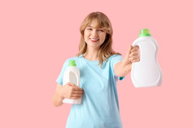 Pembe arka planda çamaşır deterjanı şişeleri olan genç bir kadın.