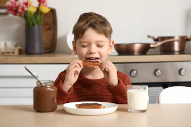 Mutfakta çikolata ezmeli tost yiyen tatlı küçük çocuk.
