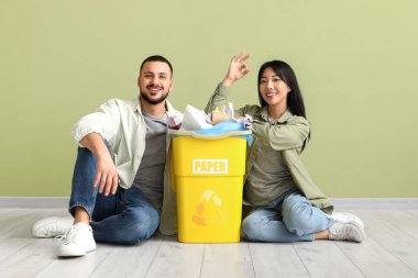 Çöp tenekelerinde yeşil duvarın yanında oturan genç çift. Küresel Geri Dönüşüm Günü