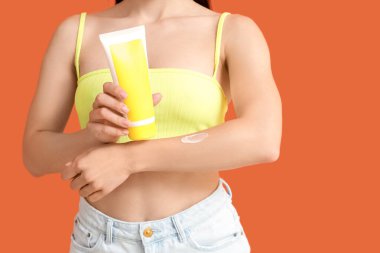 Genç bir kadın turuncu arka plana güneş kremi sürüyor, yakın plan.