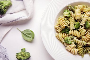 Beyaz arka planda brokoli ve fesleğen yapraklı lezzetli fusilli makarna.
