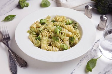 Beyaz arka planda brokoli ve fesleğen yapraklı lezzetli fusilli makarna tabağı.