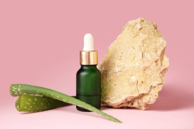 Bir şişe doğal yağ, aloe yaprakları ve pembe arka planda taş.