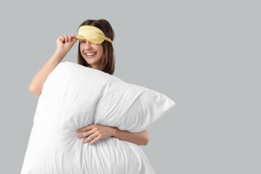 Hafif arka planda uyku maskesi ve yastığı olan genç bir kadın.