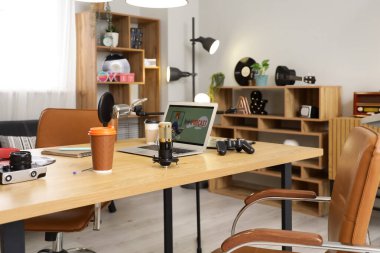 Podcaster 'ın atölyesinde dizüstü bilgisayarı, mikrofonları ve kahve fincanları olan işyeri