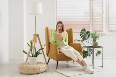 Evdeki rahat koltukta kitap okuyan şaşırmış genç bir kadın.