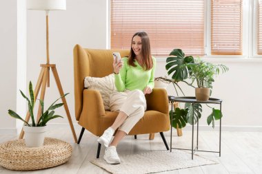 Evdeki rahat koltukta cep telefonu kullanan güzel bir kadın.