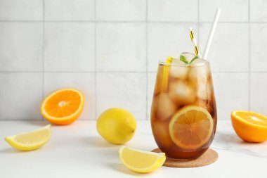 Bir bardak Long Island buzlu çay kokteyli ve beyaz masada nane ve narenciye.
