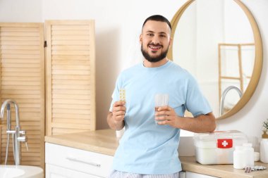 Genç adam banyoda ilk yardım çantasıyla hap alıyor.
