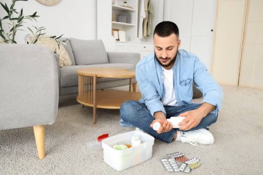 Genç adam evde ilk yardım çantasıyla ilaç alıyor.