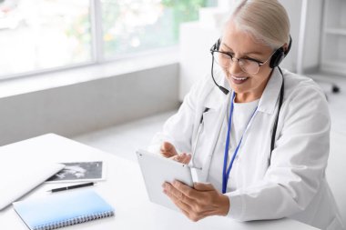 Kulaklık ve tablet bilgisayarlı kadın doktor klinikte online danışmanlık yapıyor.