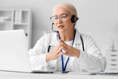 Kulaklık ve dizüstü bilgisayarı olan kadın doktor klinikte online danışmanlık yapıyor.