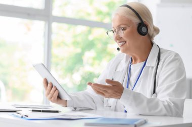 Kulaklık ve tablet bilgisayarlı kadın doktor klinikte online danışmanlık yapıyor.