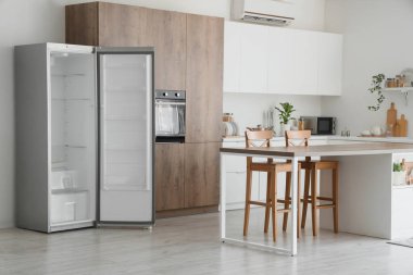 Mutfağın içi boş buzdolabı, masa ve tezgahlarla dolu.