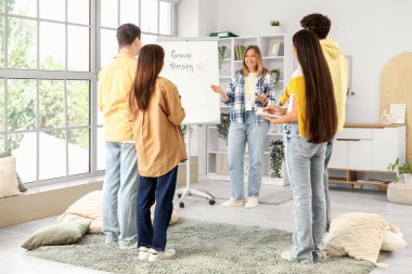 Grup terapi seansında tablonun yanında olan kadın psikolog.