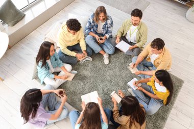 Gençler grup terapi seansında halıya not defterleri yazıyorlar.