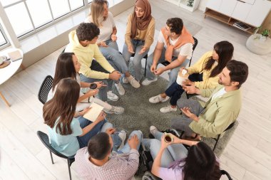 Grup terapi oturumunda sandalyede oturan gençler.