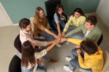 Gençler grup terapisi seansında el ele tutuşuyorlar.