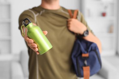 Evde su şişesi ve spor çantası olan bir adam var.