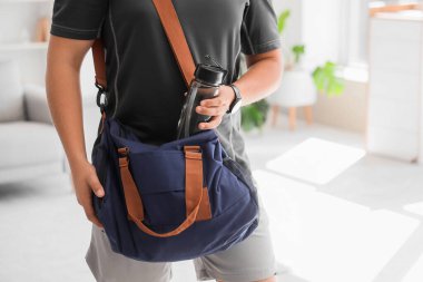 Genç adam evdeki spor çantasına su koyuyor.