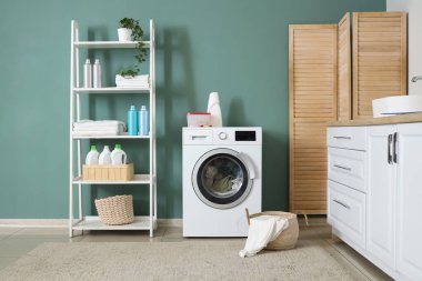 Çamaşır makinesi, raf ünitesi ve katlama ekranlı çamaşır odasının içi.