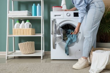 Çamaşır deterjanını kirli çamaşırlarıyla çamaşır makinesine koyan kadın.