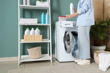 Çamaşır makinesinin yanına çamaşır deterjanı döken kadın.